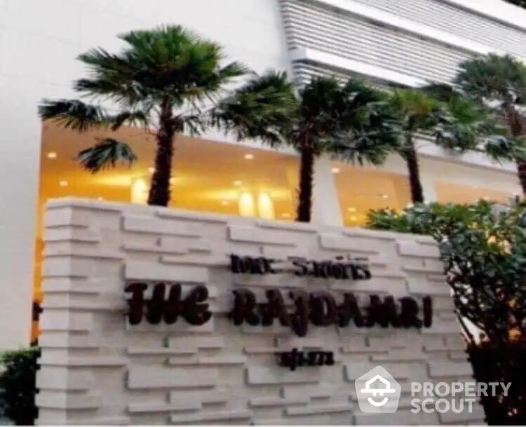 Modern building entrance with palm trees and stylish signage at The Rajdamri.