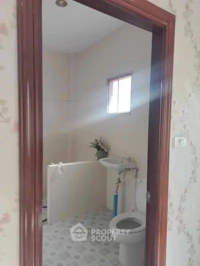 Cozy bathroom with tiled floor and natural light, featuring a toilet and sink.