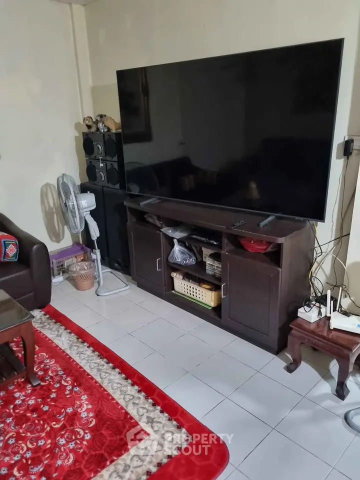 Cozy living room with large TV, elegant furniture, and vibrant red carpet.