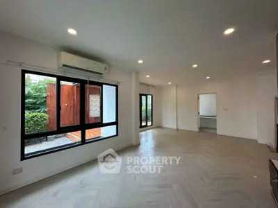 Spacious modern living room with large windows and garden view, featuring elegant wooden flooring and recessed lighting.