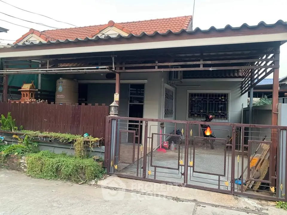 Charming single-story home with gated entrance and tiled roof, featuring a cozy front yard and traditional design.