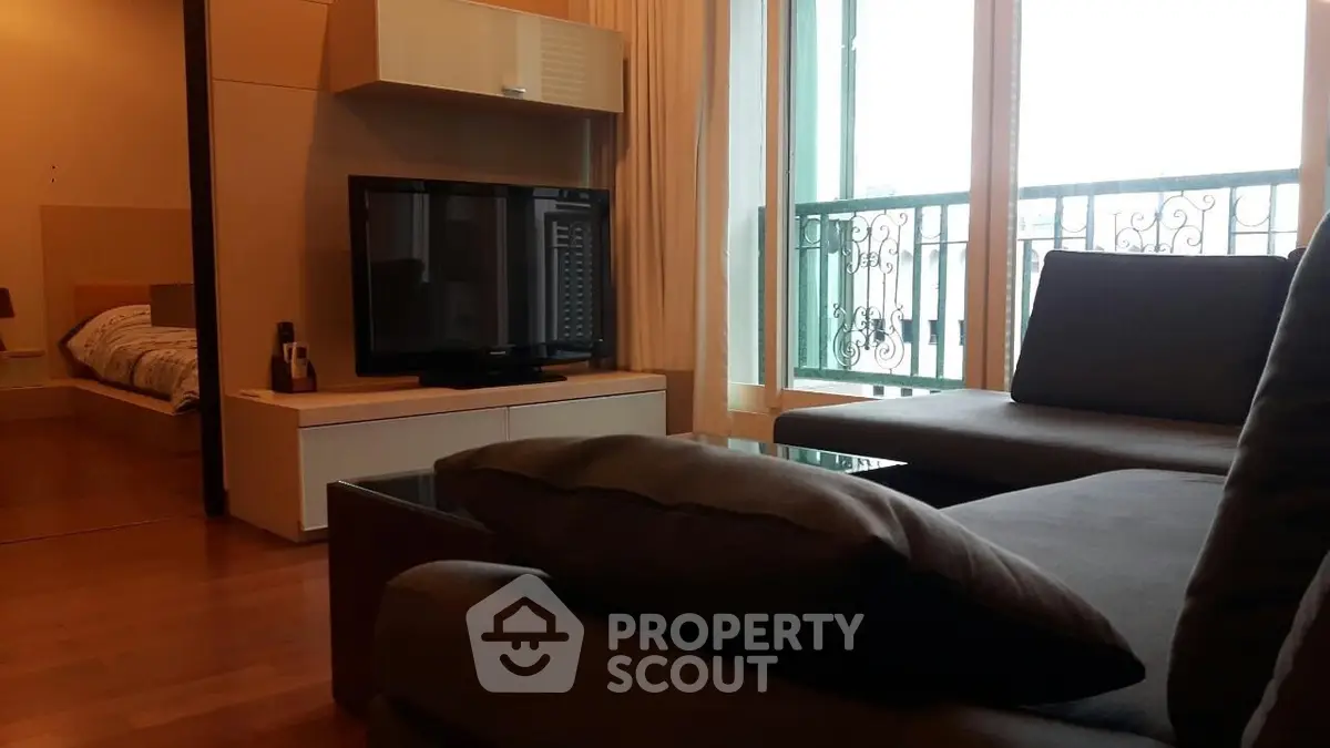 Modern living room with cozy sofa and TV, adjacent to a bedroom with balcony view.