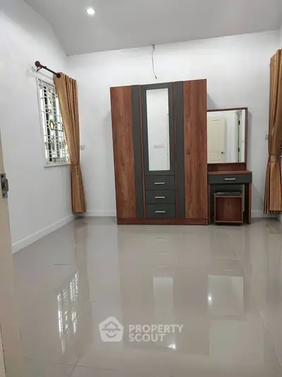 Spacious bedroom with modern wardrobe and vanity set, featuring glossy tiled flooring and elegant curtains.