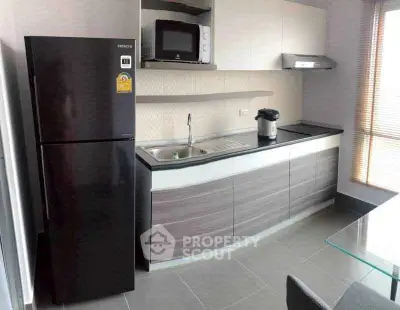 Modern kitchen with sleek cabinets, black fridge, and built-in microwave in a stylish apartment.