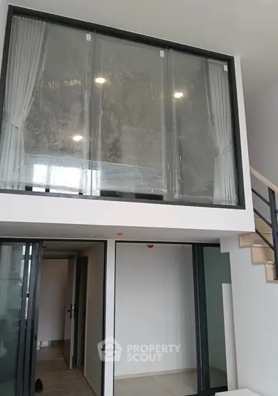 Modern duplex apartment with large windows and staircase, showcasing open and airy design.