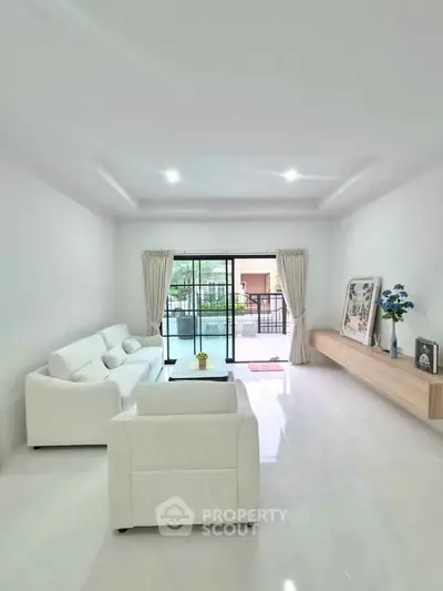 Spacious modern living room with white furniture and large windows opening to a balcony.