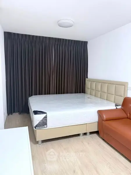 Modern bedroom with stylish bed and leather sofa, featuring elegant curtains and wooden flooring.