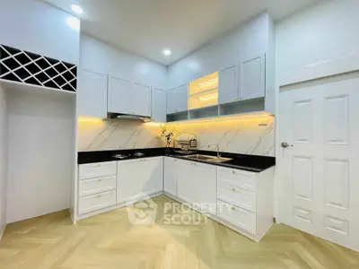 Modern kitchen with sleek white cabinets and black countertops, featuring under-cabinet lighting and a wine rack.