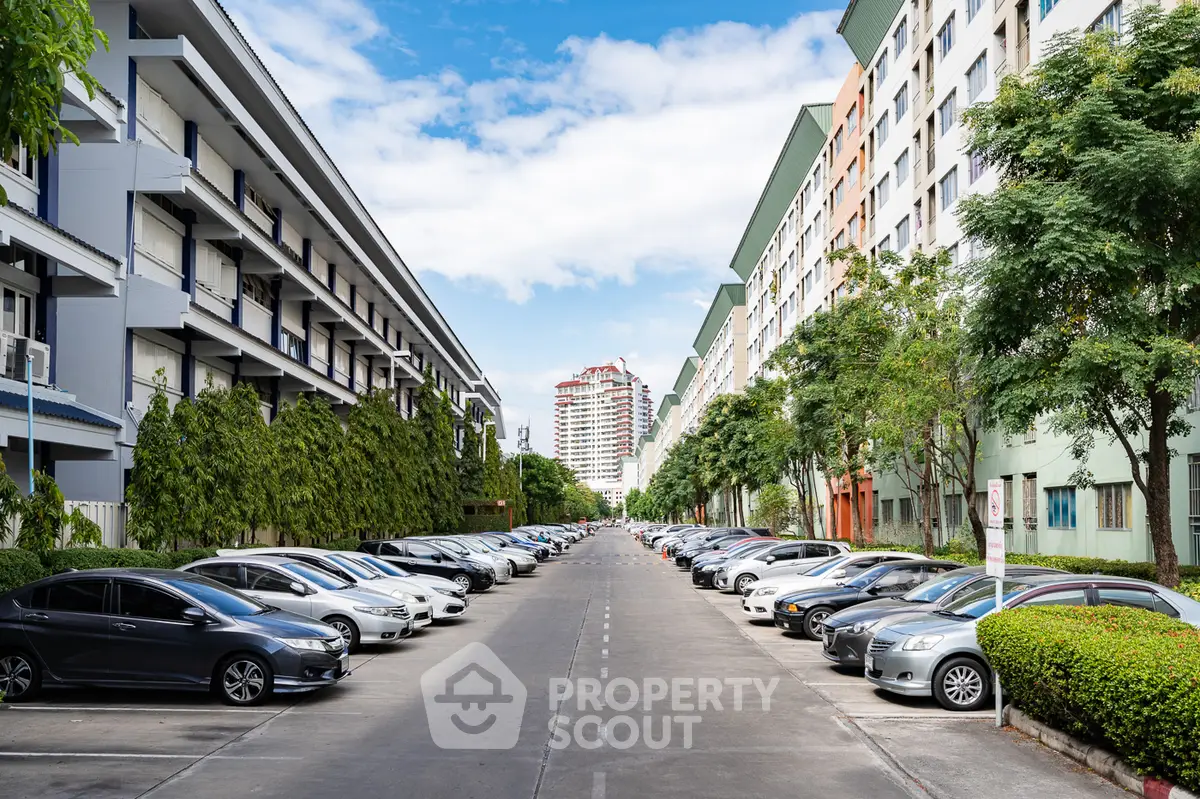 Spacious parking area between modern apartment buildings with lush greenery.