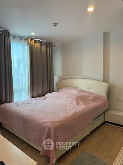 Cozy bedroom with large window and elegant curtains, featuring a comfortable bed with a pink quilt.