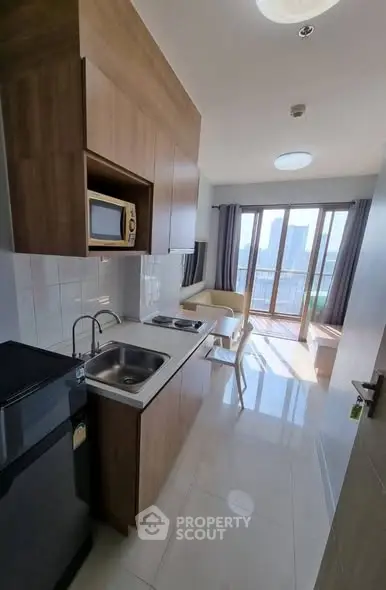 Modern compact kitchen with open layout and city view from balcony in high-rise apartment.