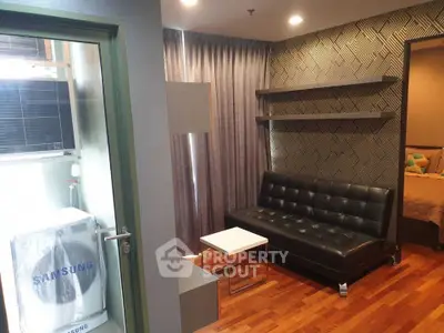 Modern living room with stylish decor and wooden flooring, featuring a sleek black sofa and elegant shelving.
