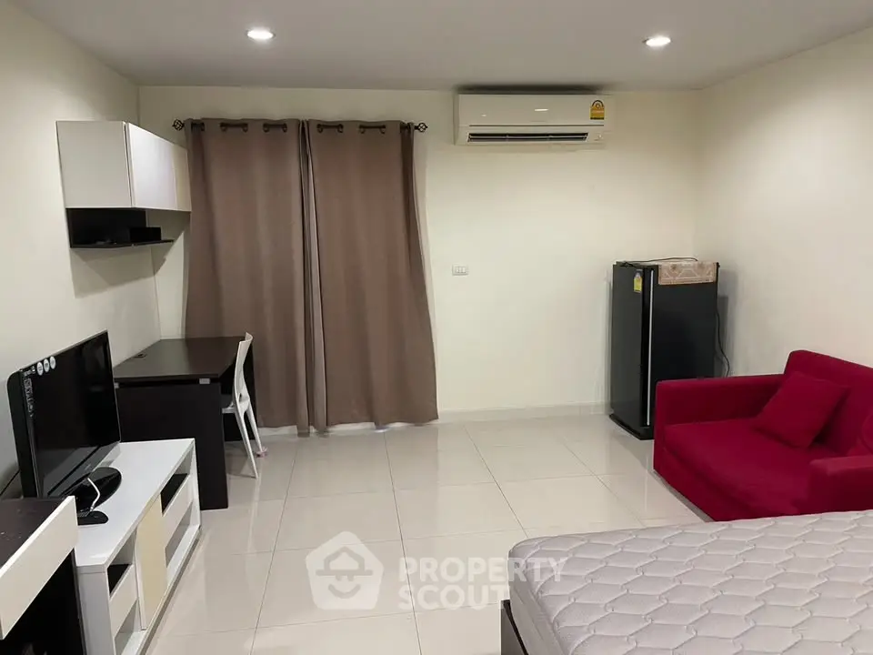 Modern studio apartment with sleek furnishings and air conditioning, featuring a cozy red sofa and compact fridge.