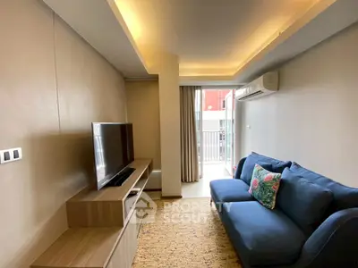 Modern living room with cozy blue sofa and flat-screen TV, featuring elegant lighting and balcony access.