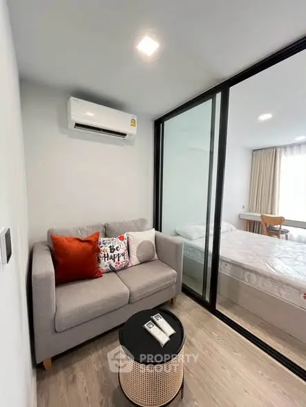 Modern compact living room with cozy sofa and glass partition to bedroom