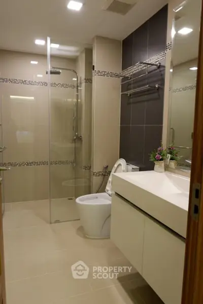 Modern bathroom with glass shower and sleek vanity in contemporary apartment.