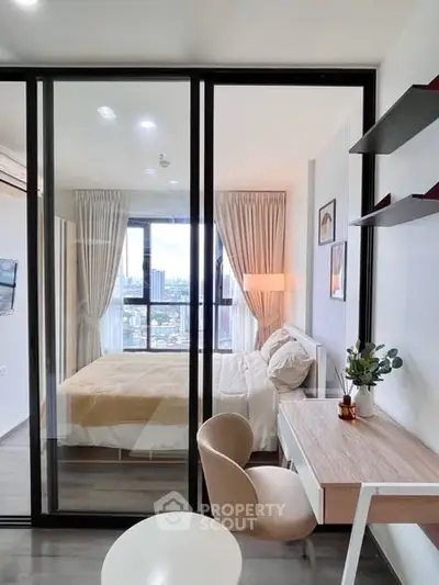 Modern bedroom with glass partition and city view, featuring a cozy study area and elegant decor.