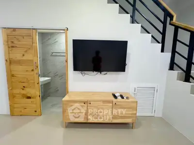 Modern living room with wooden sliding door, wall-mounted TV, and sleek staircase design.