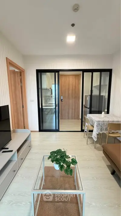 Modern living room with sliding glass doors leading to a sleek kitchen, featuring stylish decor and natural light.