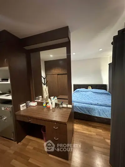 Cozy bedroom with wooden flooring and built-in storage, featuring a comfortable bed and a small vanity area.