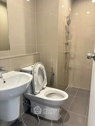 Modern bathroom with sleek fixtures and neutral tiles, featuring a shower and toilet.