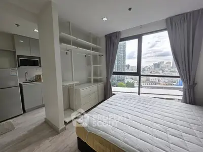Modern bedroom with large window and city view, featuring open closet and adjacent kitchen area.