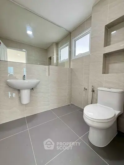 Modern bathroom with sleek fixtures and neutral tiles, featuring a wall-mounted sink and toilet.