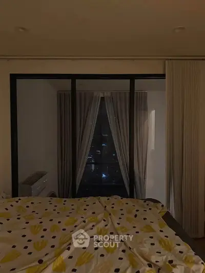 Cozy bedroom with city view through large window and stylish bedding.
