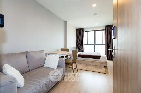 Modern studio apartment with cozy living area and bed, featuring large windows and stylish decor.