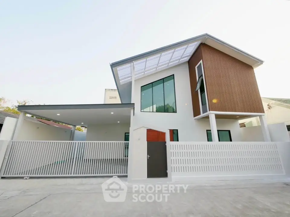 Modern two-story house with sleek design and spacious carport, featuring large windows and a stylish facade.