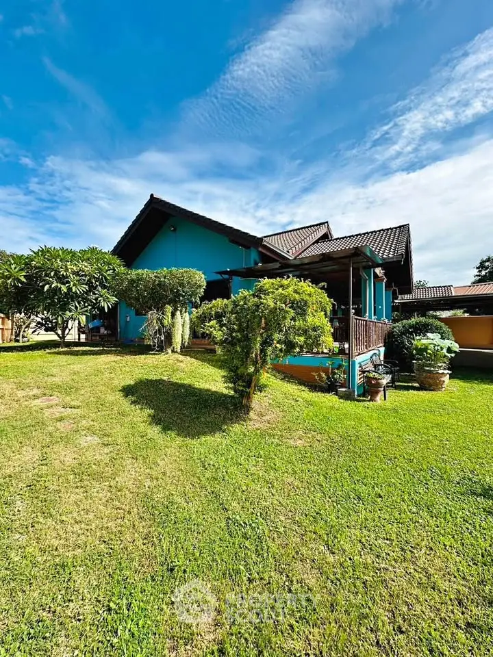 Charming blue house with lush garden and spacious lawn under a clear blue sky.