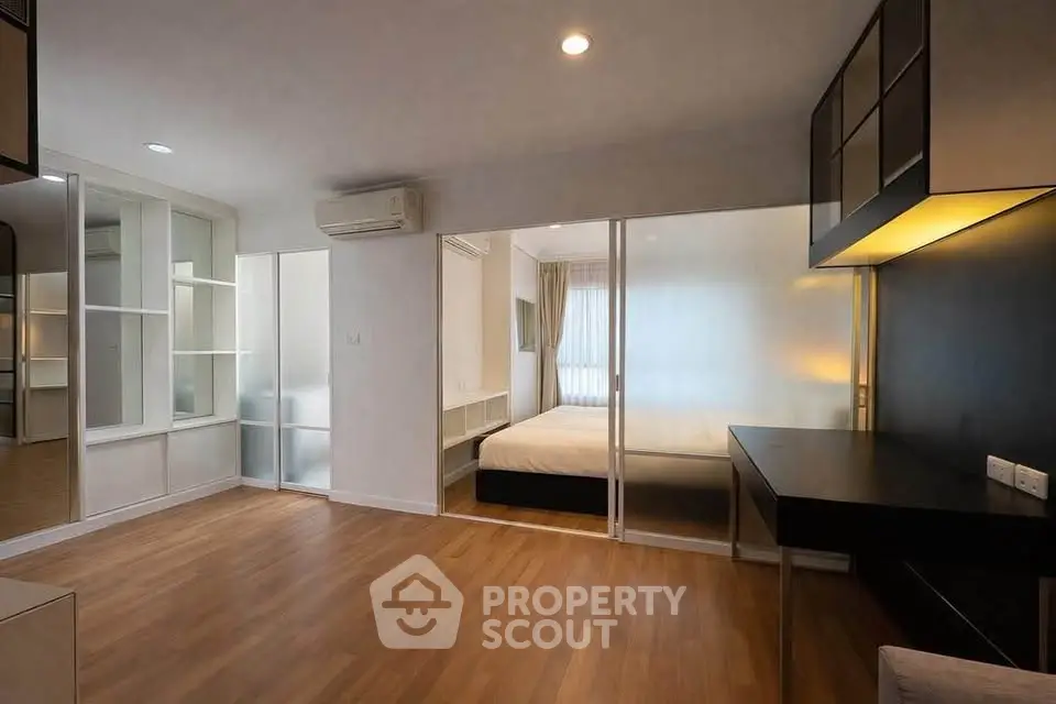 Modern apartment interior with wooden flooring, sliding glass doors, and built-in storage solutions.