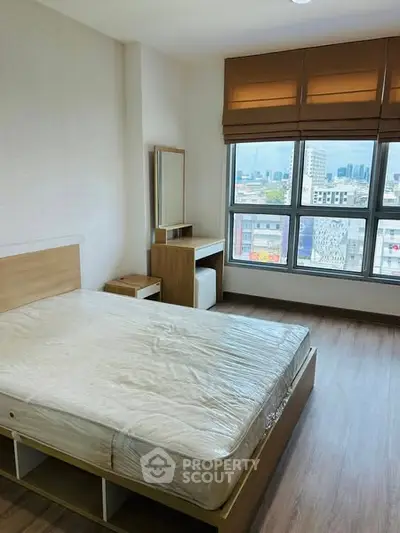 Spacious bedroom with large window offering city views, featuring modern furnishings and wooden flooring.