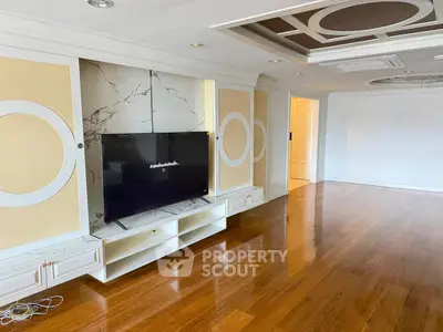 Spacious living room with elegant ceiling design and hardwood floors, featuring a modern TV setup.