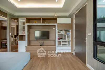 Modern living room with built-in wooden shelves and TV, featuring elegant decor and ample natural light.