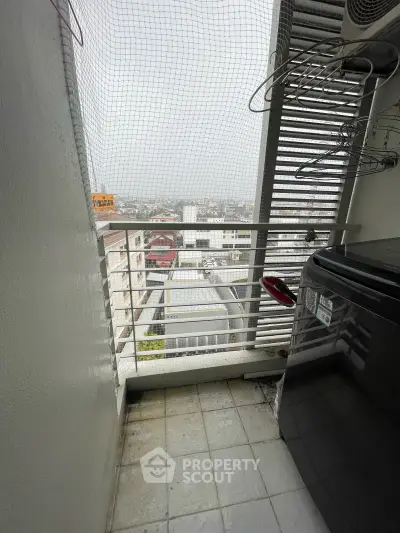 Compact balcony with city view, featuring a washing machine and protective netting, ideal for urban living.
