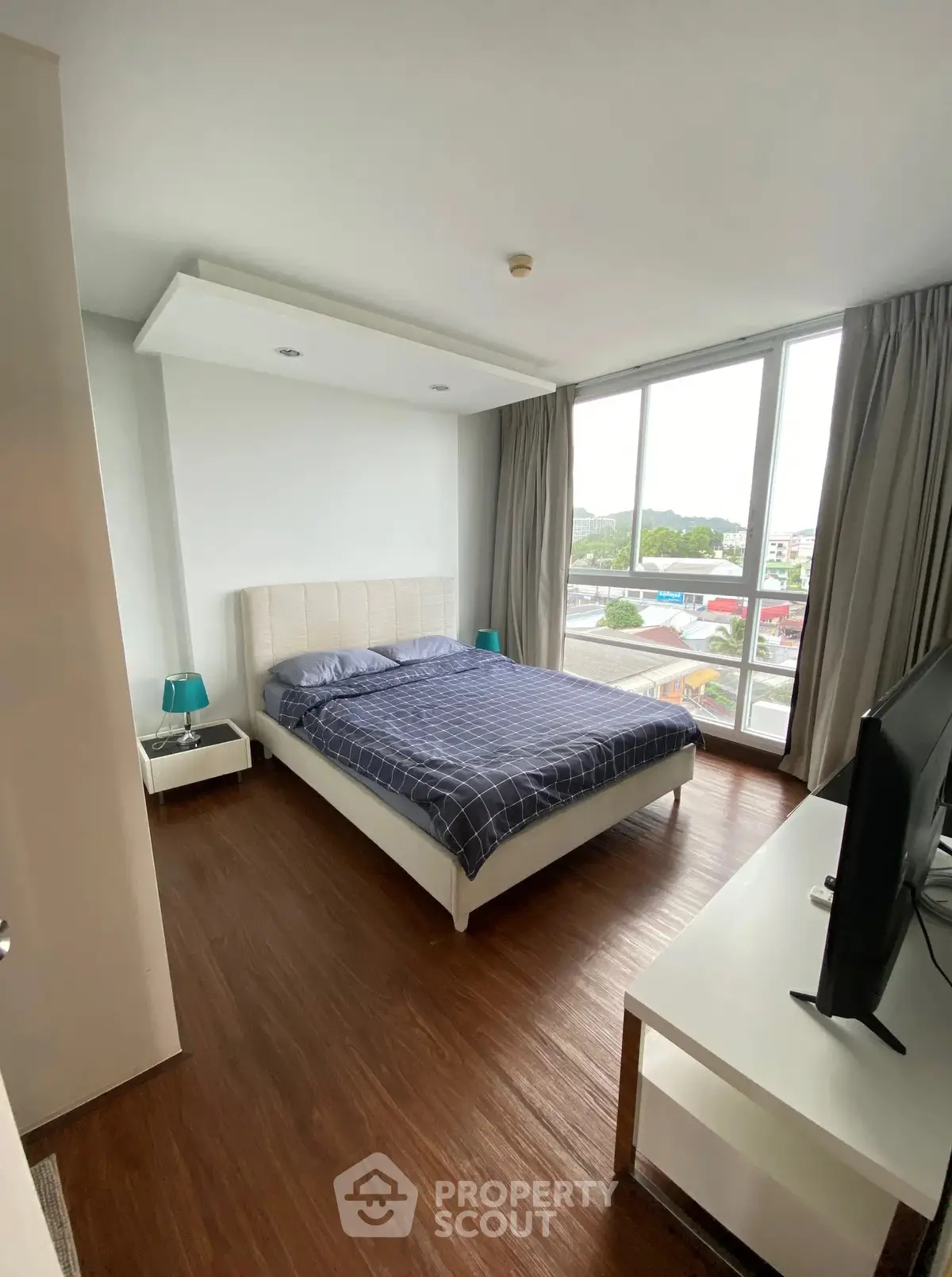 Modern bedroom with large windows and wooden flooring offering a bright and cozy atmosphere.