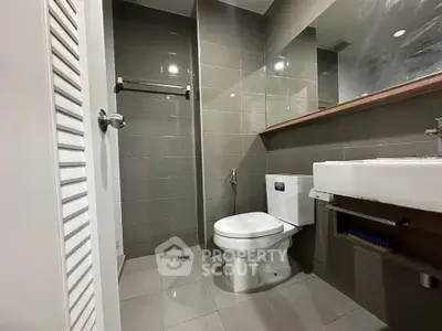 Modern bathroom with sleek design and neutral tiles, featuring a toilet and wall-mounted sink.