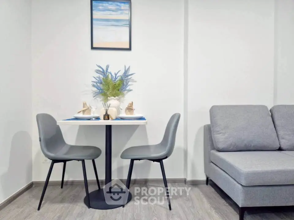 Modern living room with stylish gray sofa and elegant dining table set for two, featuring contemporary decor.