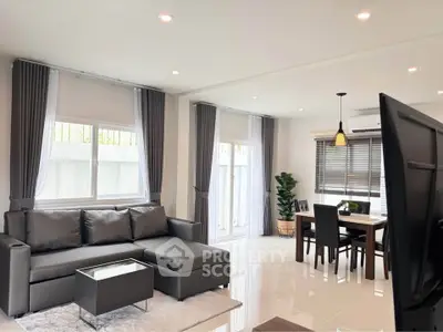Modern living room with sleek furniture and dining area, featuring large windows and elegant decor.