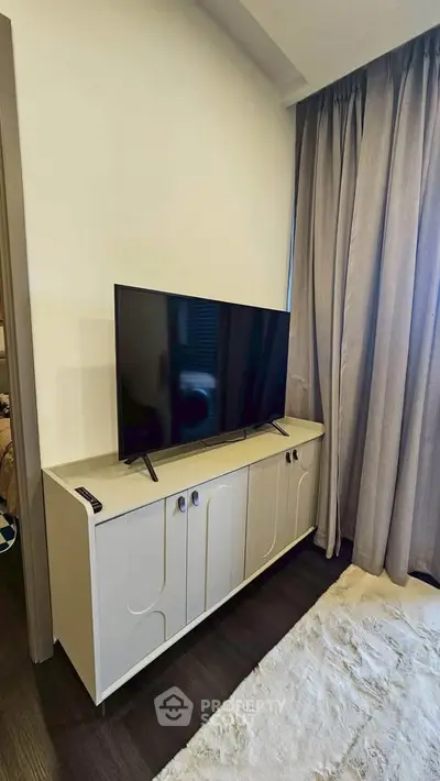 Modern living room with sleek TV stand and large flat-screen TV, complemented by elegant curtains and plush rug.