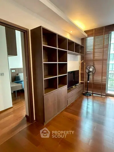 Modern living room with wooden flooring and built-in shelving, featuring a sleek design and natural light.