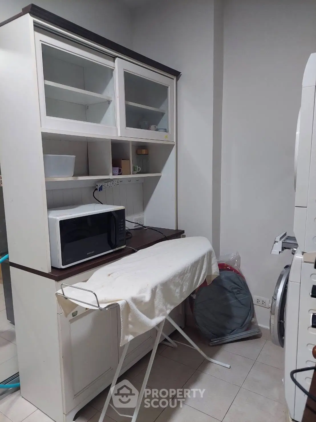Compact kitchen with microwave and laundry area, featuring a modern washing machine and storage cabinet.
