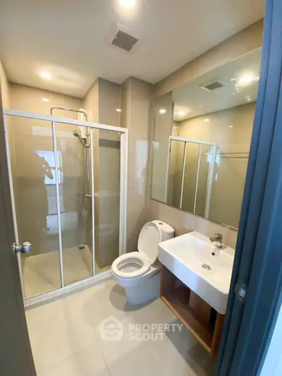 Modern bathroom with glass shower, sleek sink, and toilet in contemporary apartment.