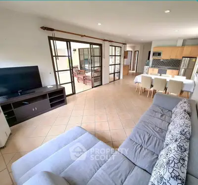 Spacious open-plan living room with modern kitchen and dining area, featuring large windows and stylish decor.