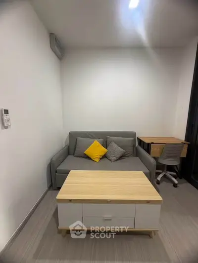 Cozy living room with modern sofa, stylish coffee table, and workspace in a compact apartment.