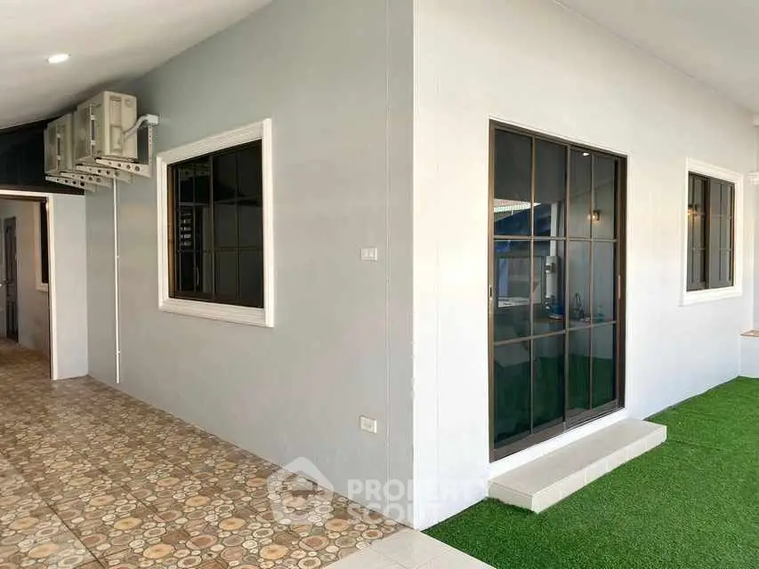 Modern exterior with tiled walkway and artificial grass, featuring large windows and air conditioning unit.