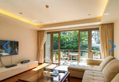 Spacious living room with large windows opening to a sunny balcony with garden view.