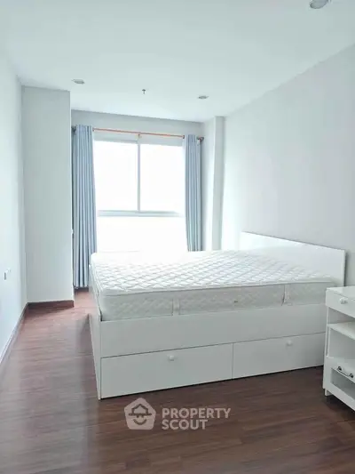 Bright and airy bedroom with large window and modern white furniture, perfect for relaxation.