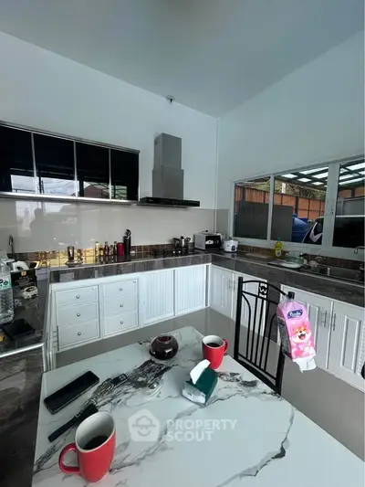 Modern kitchen with marble countertops and sleek cabinetry, featuring a gas stove and ample natural light.